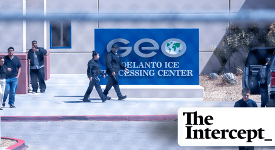 A photo through a chain-link fence. People in dark blue uniforms walk past a large sign that reads "GEO Delanto ICE Processing Center." Bottom right, the logo for the Intercept. 